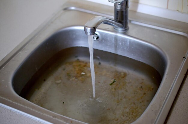 Foto el agujero del tapón del fregadero de acero inoxidable se cierra lleno de agua y partículas de comida