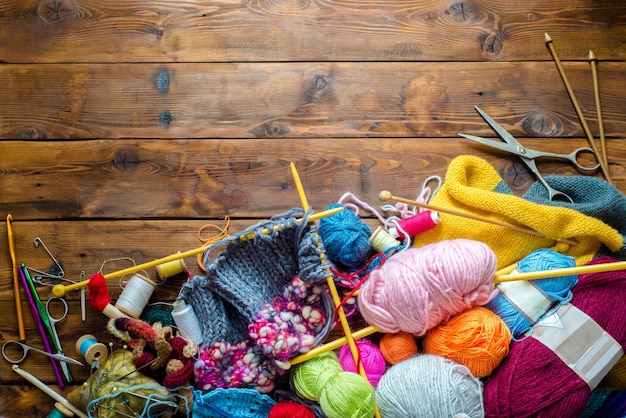 Agulhas de tricô bolas de lã e outras ferramentas vistas de cima em uma mesa de madeira com muitas ferramentas