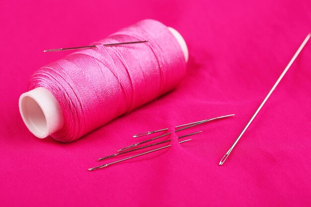 Foto agulhas e bobinas de fio em fundo de tecido de cor