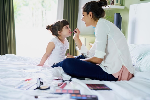 Ahora las dos nos vemos exactamente iguales Toma de una madre y su hijita jugando con el maquillaje en la cama de su casa