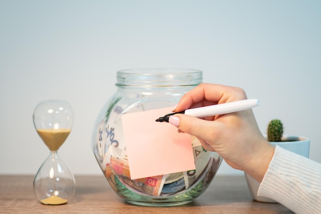 Foto ahorrar dinero en ucrania jar con dinero de hryvnia y papel en blanco escribiendo inscripción con marcador