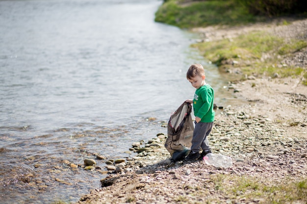 Ahorre el concepto del medio ambiente, un niño pequeño que recoge basura y botellas de plástico en la playa para tirar a la basura.