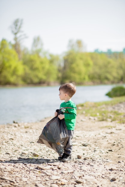 Ahorre el concepto del medio ambiente, un niño pequeño que recoge basura y botellas de plástico en la playa para tirar a la basura.