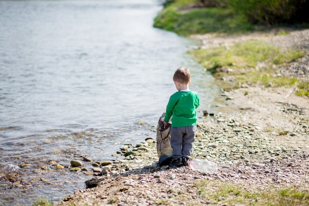 Ahorre el concepto del medio ambiente, un niño pequeño que recoge basura y botellas de plástico en la playa para tirar a la basura.