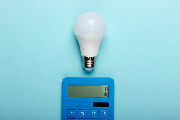 El ahorro de energía. Calculadora con bombilla led sobre un fondo azul pastel. Vista superior