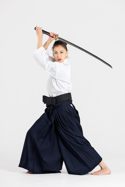 Aikido-meisterfrau im traditionellen samurai-hakama-kimono mit schwarzem gürtel mit schwert katana auf weiß