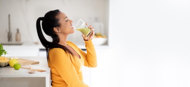 Ainda bem que a jovem vegana afro-americana à mesa com vegetais orgânicos bebe smoothie fresco no copo