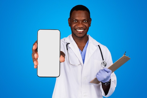 Ainda bem que o jovem médico afro-americano de jaleco branco com prancheta mostra smartphone vazio