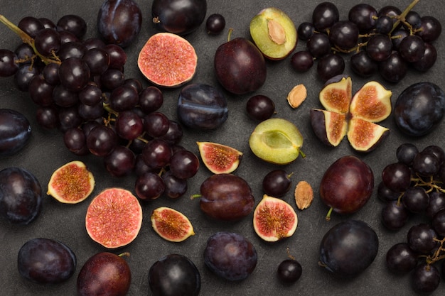Ainda vida de frutas. Cacho de uvas. Figos e ameixas. Corte figos, metades de ameixa, caroços de ameixa. Fundo preto. Postura plana