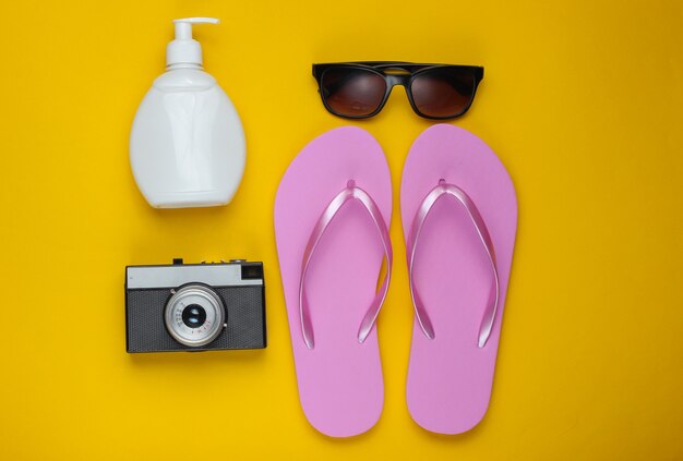 Ainda vida de verão. acessórios de praia. flip-flops rosa praia na moda, câmera retro, frasco de protetor solar, óculos de sol, concha em fundo de papel amarelo.