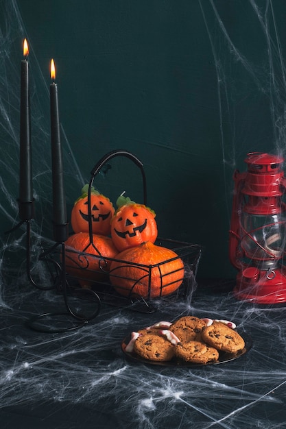 Foto ainda vida sobre o tema do feriado de halloween. sobre a mesa está uma cesta de abóboras, duas velas pretas, um prato de biscoitos. a mesa está emaranhada em teias de aranha.