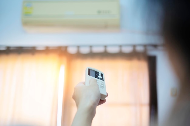 Foto un aire acondicionado en una habitación con una persona joven usando un control remoto está encendiendo el aire