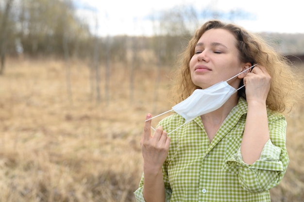 El aislamiento final y el concepto de cuarentena del virus corona covid-19. joven europea de 30 años se quita una máscara médica de la cara y respira aire fresco en la naturaleza al aire libre