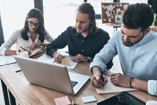 Ajetreado día de trabajo. Vista superior de jóvenes modernos en ropa casual elegante escribiendo algo