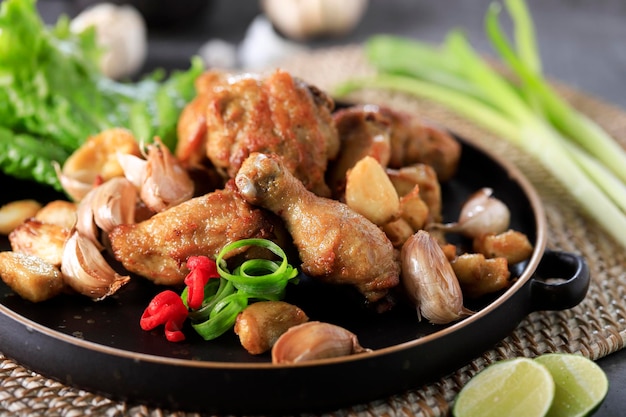 Ajo de pollo o Ayam Goreng Bawang Khas Batam, Indonesia. Pollo Frito con Ajo Especial Sazonado de Influencia China. Servido en Plato Negro con Leetuce