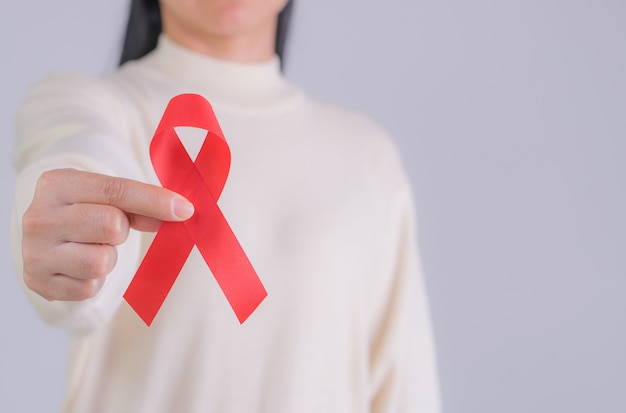 Ajuda à fita vermelha na mão da mulher para o dia mundial da Aids e o conceito nacional de HIV / AIDS e mês de conscientização do envelhecimento. Copie o espaço.