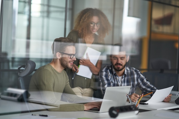 Foto ajudar três jovens colegas de trabalho felizes usando laptop e discutindo trabalho ou compartilhando novidades