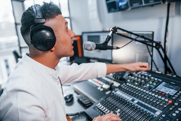 Foto ajustando el equipo el joven está adentro en el estudio de radio está ocupado por la transmisión