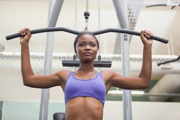 Ajustar a mulher usando a máquina de pesos para os braços dela