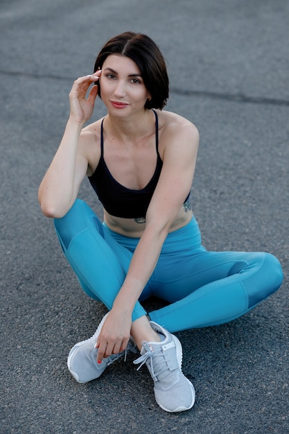 Ajuste a jovem mulher sentada ao ar livre após a sessão de treino da manhã. Modelo de fitness feminino relaxando e olhando para a câmera.