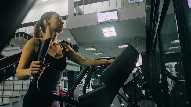 Ajuste a mulher atlética exercitando em uma máquina elíptica. Treinamento de Atividade de Mulheres Musculares no Ginásio Moderno. Treino em um treinador de caminhada elíptica.