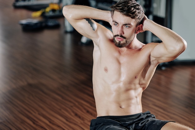 Ajuste atractivo sin camisa joven haciendo abdominales en el gimnasio