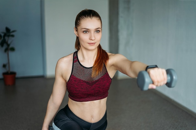 Ajuste atractivo joven en ropa deportiva niña sonriente trenes con pesas en el estudio loft