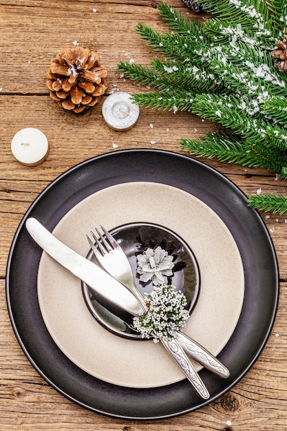 Ajuste de lugar de jantar de natal e ano novo. galho de árvore perene do abeto, velas, cones, pratos de cerâmica, garfo e faca.