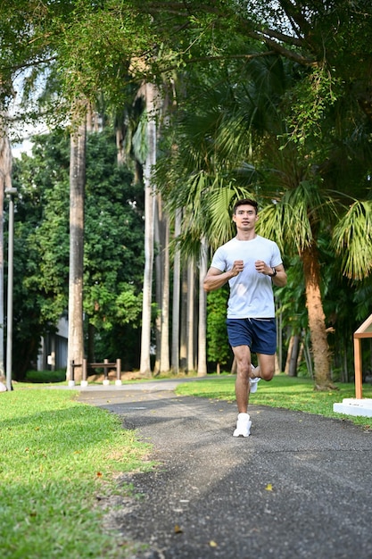 Ajuste deportivo y apuesto hombre asiático en ropa deportiva corriendo en el hermoso parque verde