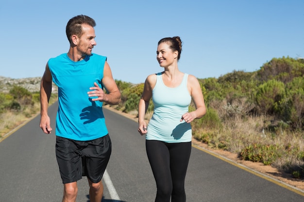 Ajuste feliz pareja corriendo juntos en la carretera