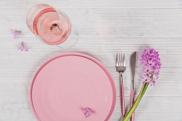 Ajuste de lugar rústico rosa con flor de jacinto púrpura y servilleta de lino y copa de vino rosado sobre fondo de madera blanca