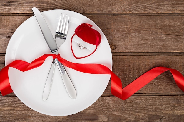 Ajuste de la mesa del día de san valentín con plato tenedor cuchillo anillo de corazón rojo y fondo de cinta