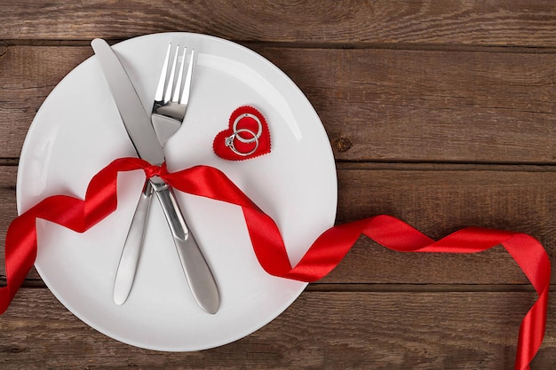 Ajuste de la mesa del día de san valentín con plato tenedor cuchillo anillo de corazón rojo y fondo de cinta
