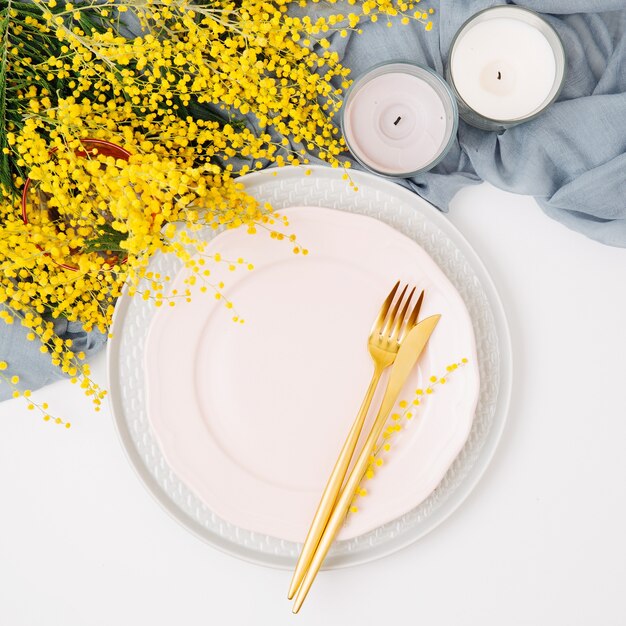 Ajuste de la mesa festiva. Platos y cubiertos con textil decorativo gris y flores amarillas sobre fondo blanco. Hermoso arreglo plano.