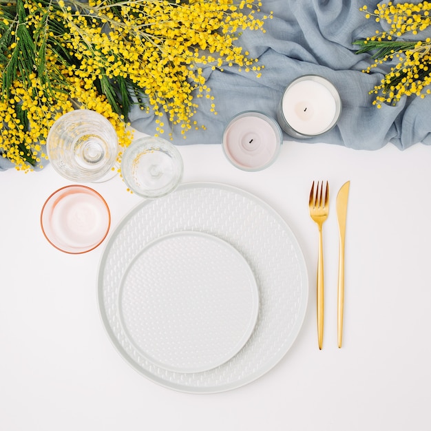 Ajuste de la mesa festiva. Platos y cubiertos con textil decorativo gris y flores amarillas sobre fondo blanco. Hermoso arreglo plano.