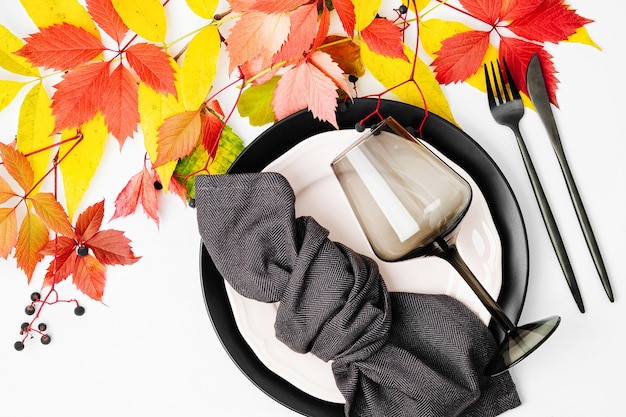 Ajuste de la mesa festiva con platos negros y copa de vino y hojas de otoño brillantes