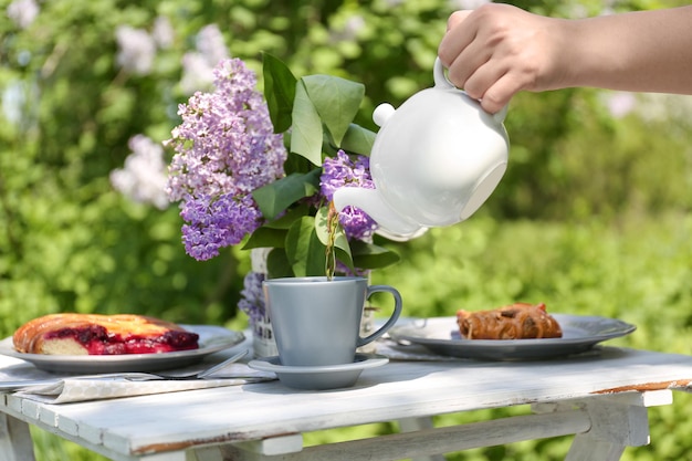 Ajuste de la mesa con flores lilas y mano femenina vertiendo té en una taza