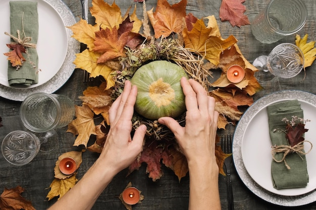 Ajuste de la mesa de otoño Las manos hacen un arreglo de otoño con calabaza para la fiesta de acción de gracias