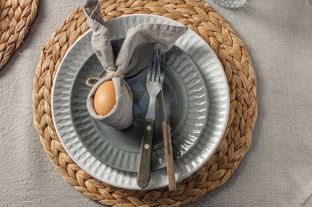 Ajuste de la mesa de Pascua festiva Divertido conejito de Pascua hecho de huevo y servilleta de lino en la placa Fondo gris