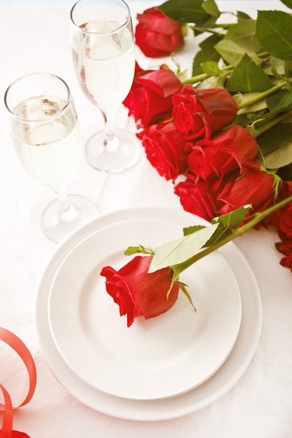 Ajuste de la mesa del restaurante romántico para dos con rosas, platos y vasos.