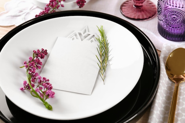 Ajuste de la mesa con tarjeta en blanco de servilleta de color crema y decoración floral lila en superficie de madera