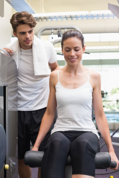 Ajuste morena usando la máquina de pesas para las piernas con el entrenador viendo