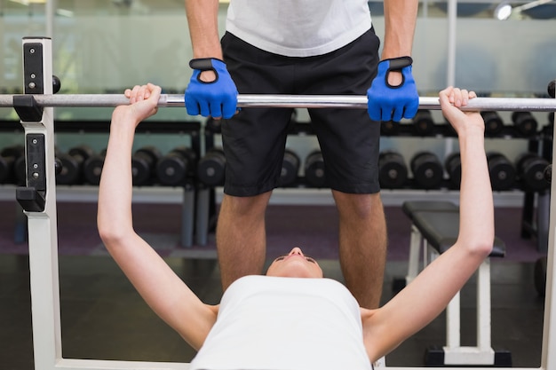 Ajuste a la mujer que levanta la barra con su instructor que detecta en el gimnasio