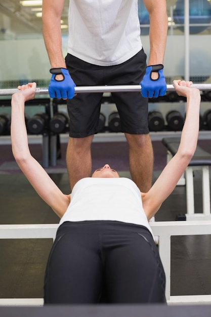 Ajuste a la mujer que levanta la barra con su instructor que mancha