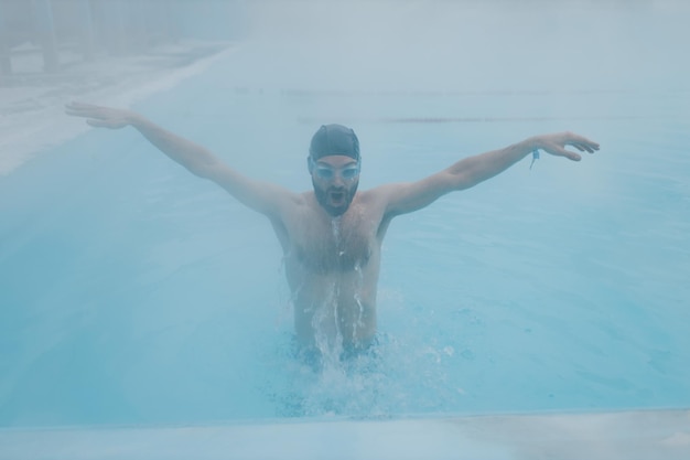 Ajuste nadador entrenamiento masculino nadar en piscina abierta de invierno con niebla Concepto de spa geotérmico al aire libre