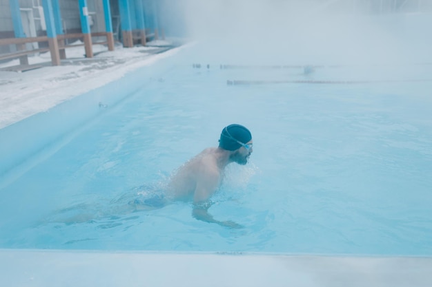 Ajuste nadador entrenamiento masculino nadar en piscina abierta de invierno con niebla Concepto de spa geotérmico al aire libre