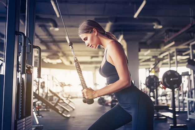 Ajuste o tríceps de treino de mulher levantando pesos no ginásio. Mulher sexy atlética fazendo exercício usando máquina no ginásio.