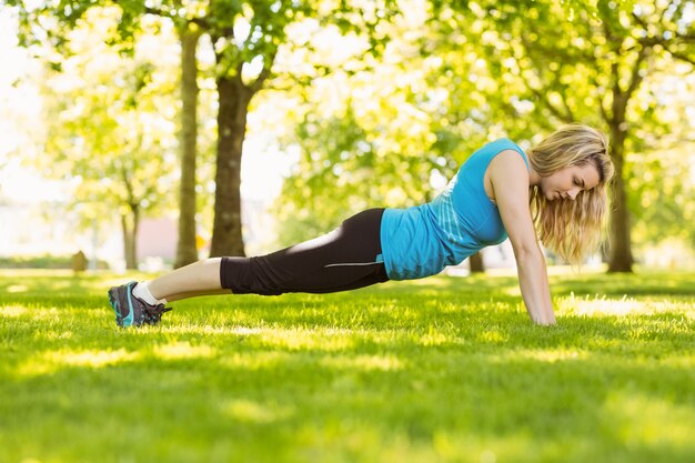 Ajuste rubia haciendo flexiones en el parque