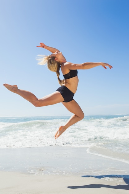 Ajuste rubia saltando con gracia en la playa