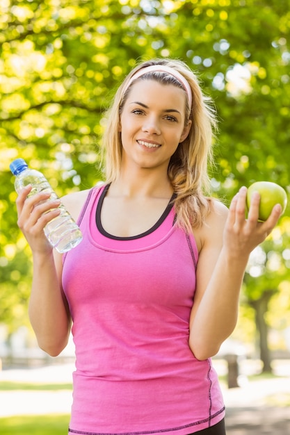 Ajuste rubia sosteniendo agua y manzana